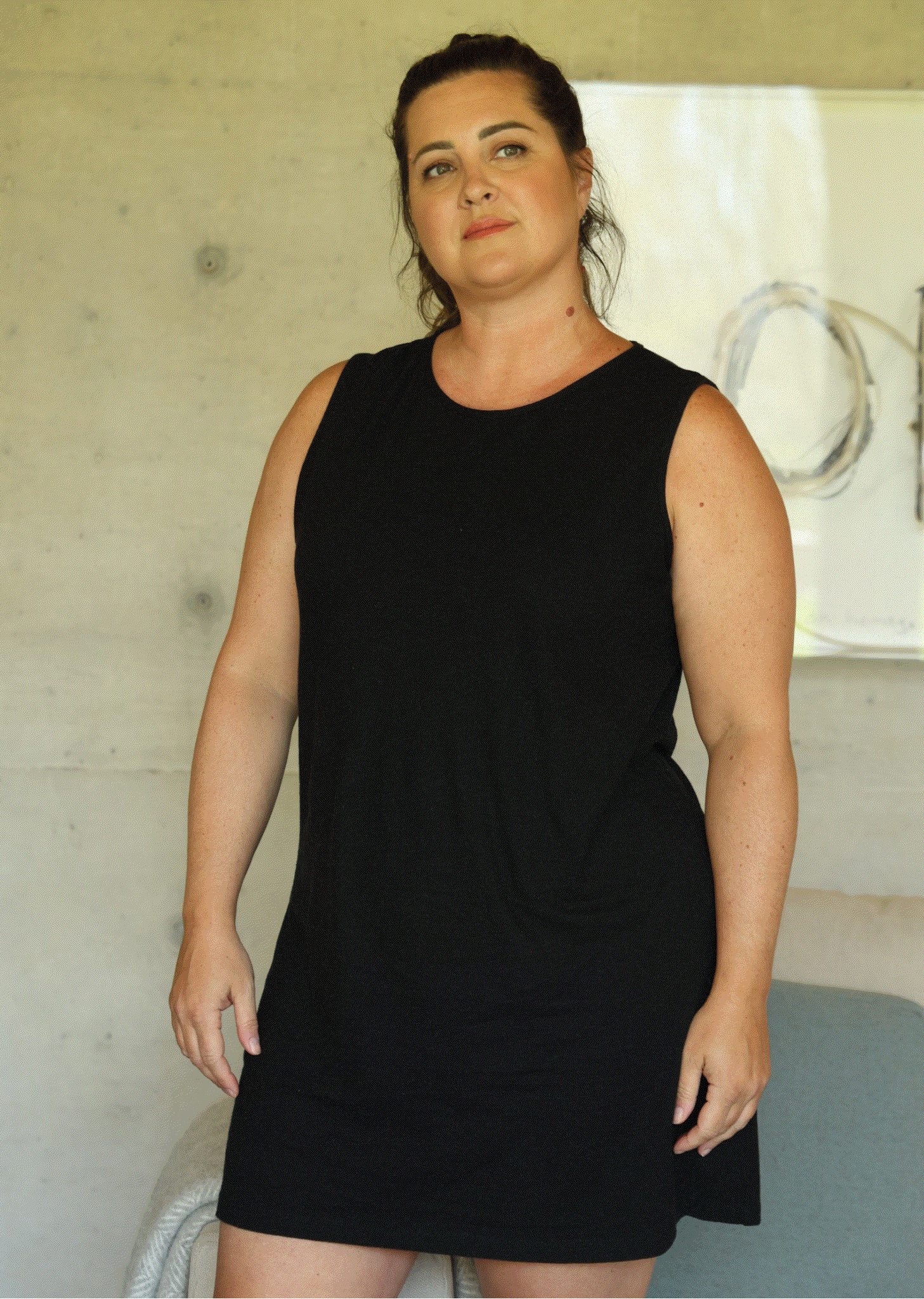 Woman wearing a black sleeveless dress indoors.