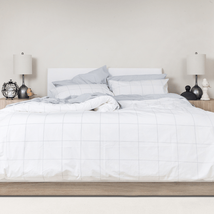 Neatly made bed with white cotton bedding and light blue pillows in a bedroom setting.