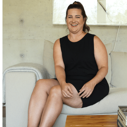 Woman in a black cooling nightgown for women sitting on a couch in a bright room.