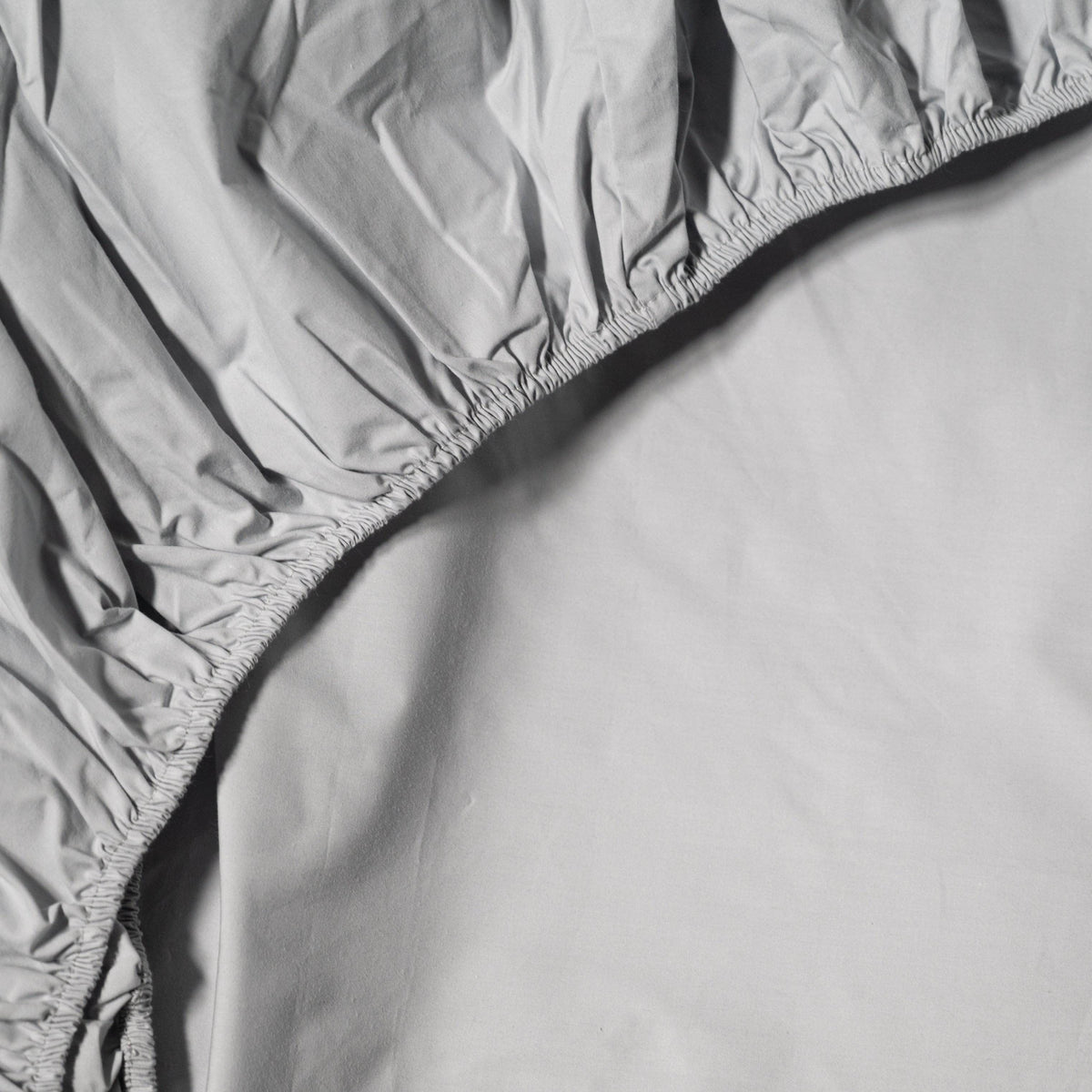Gray fitted cotton sheet on a bed with a plain background