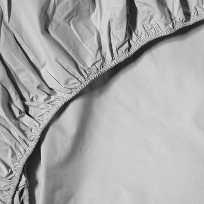 Gray fitted cotton sheet on a bed with a plain background