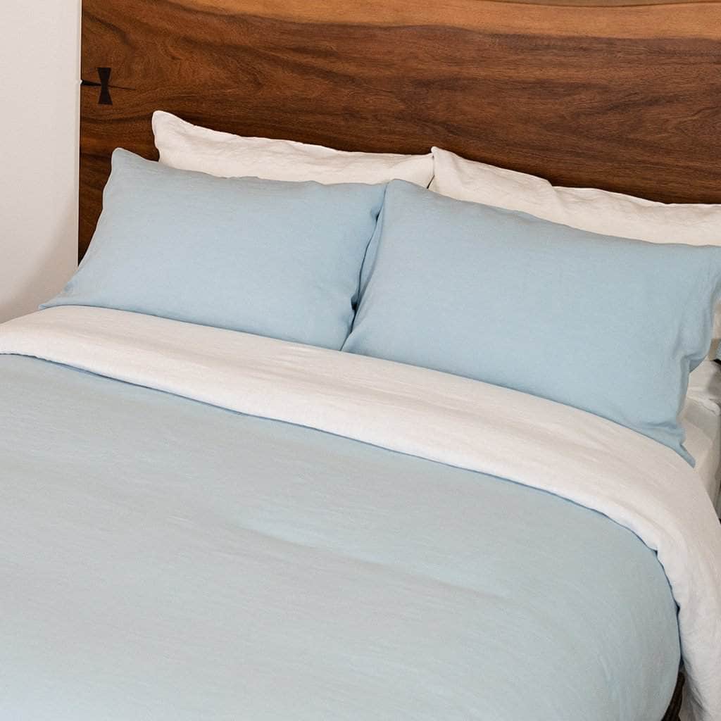 Light blue bedding set with white trim on a bed with a wooden headboard.