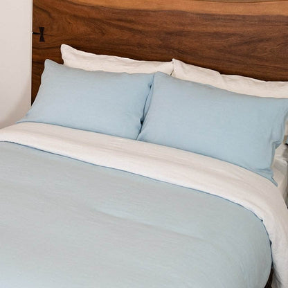 Light blue bedding set with white trim on a bed with a wooden headboard.