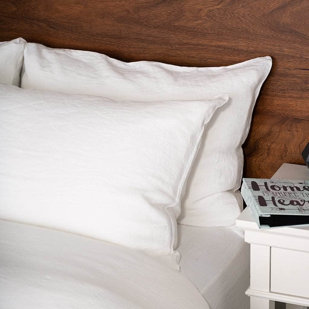 White linen sheet pillows on a bed with a wooden headboard and a nightstand with a book.