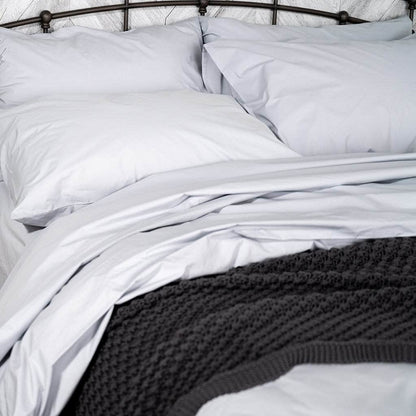 White organic cotton bedding on a bed with a dark headboard