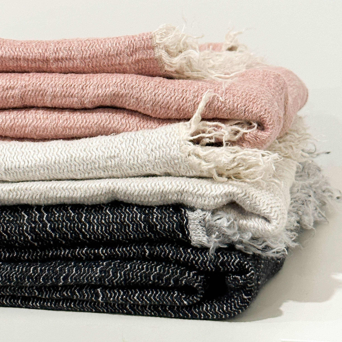 Stack of folded blankets in pink, white, and black on a light background