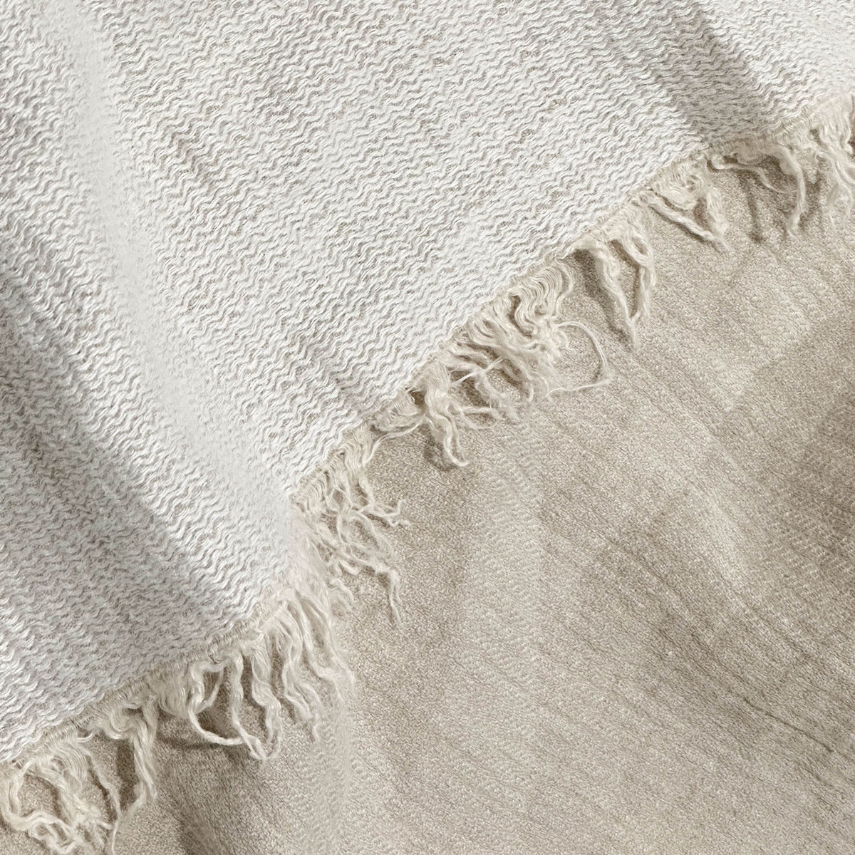 Close-up of a textured beige linen throw blanket with frayed edges on a light background