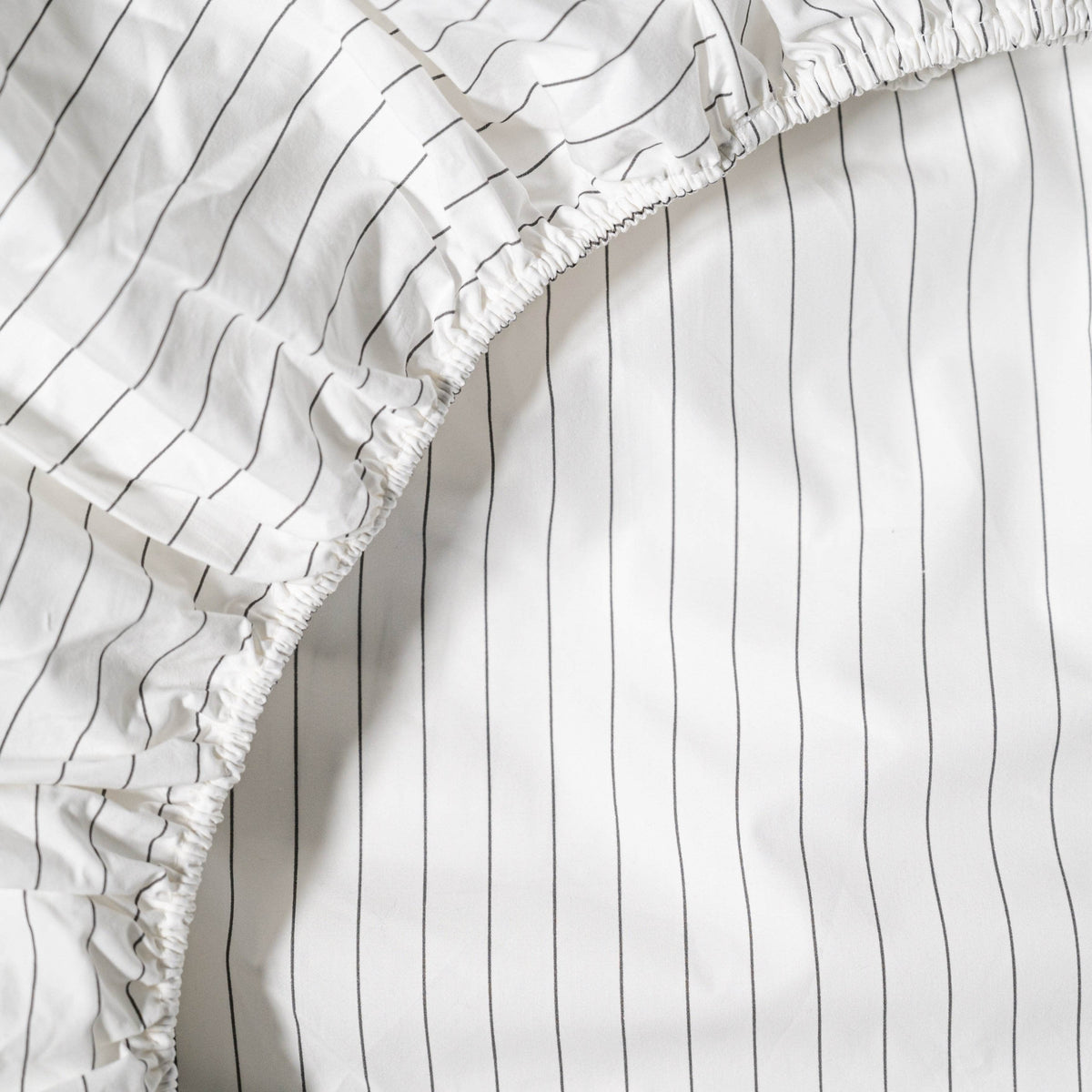 Close-up of a white cotton sheets with black vertical stripes and ruffled edge.