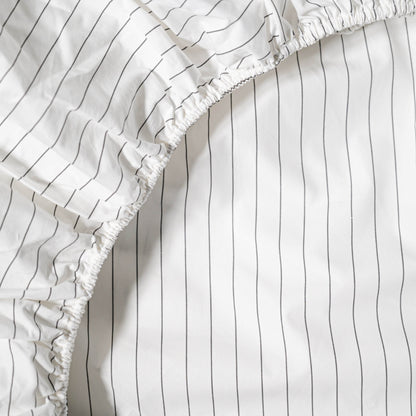 Close-up of a white cotton sheets with black vertical stripes and ruffled edge.